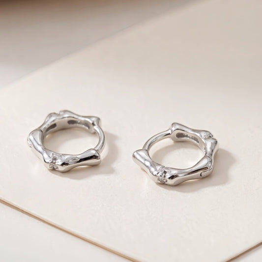 Silver Noma organic huggie earrings on a white background
