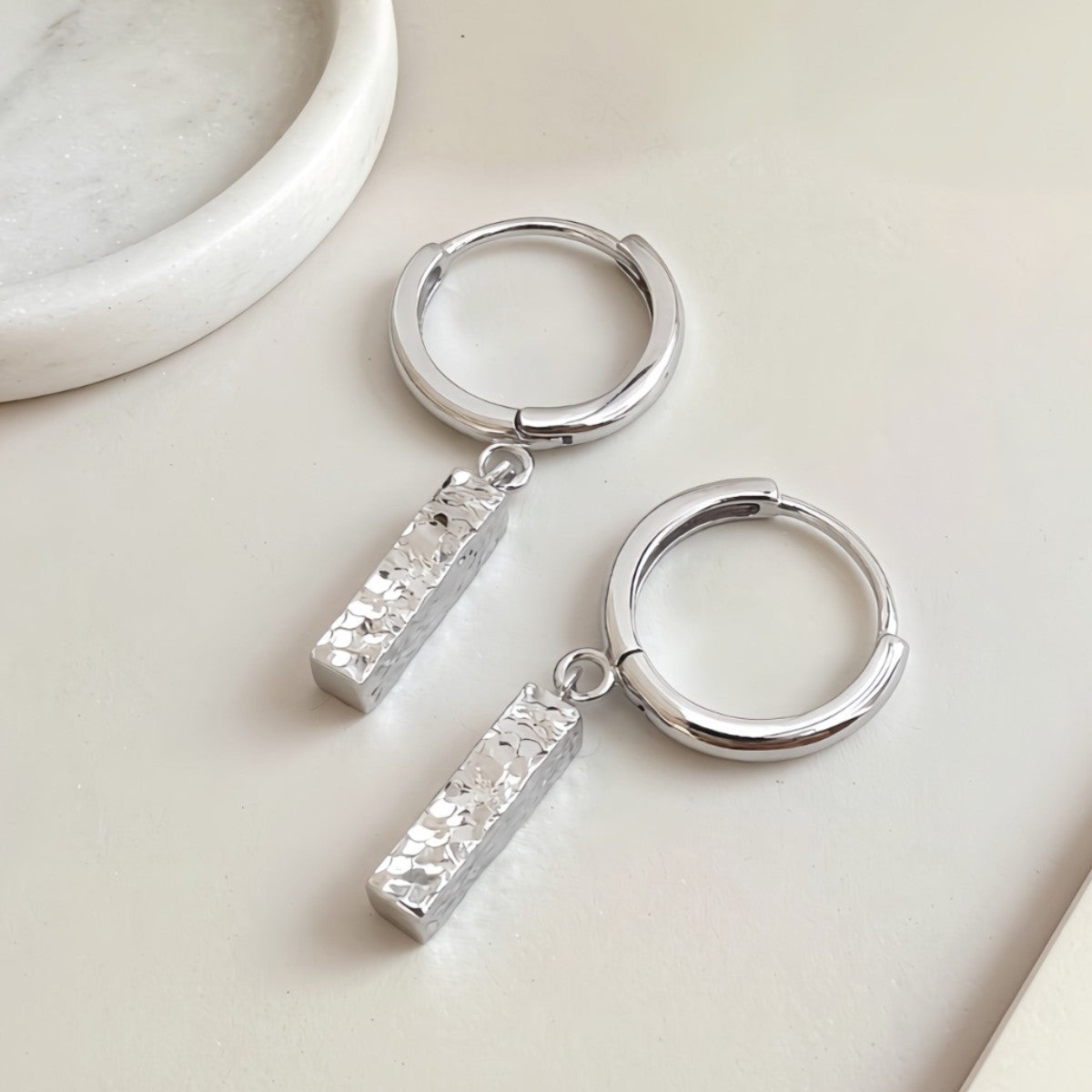 Silver Sora hammered bar drop earrings on a light surface