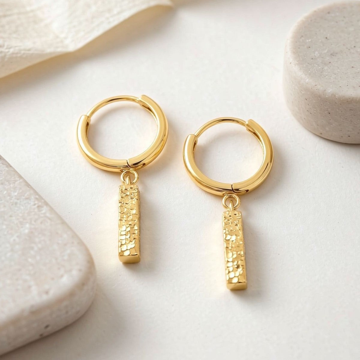 Gold Sora hammered bar drop earrings on a light surface