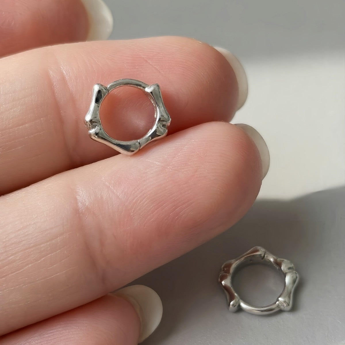 Silver Noma organic huggie earring held between fingers