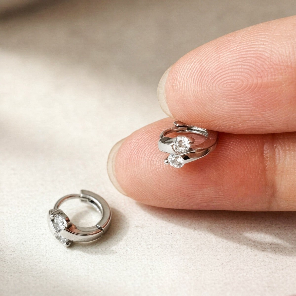 Silver Lumi double CZ huggie earring held between fingers