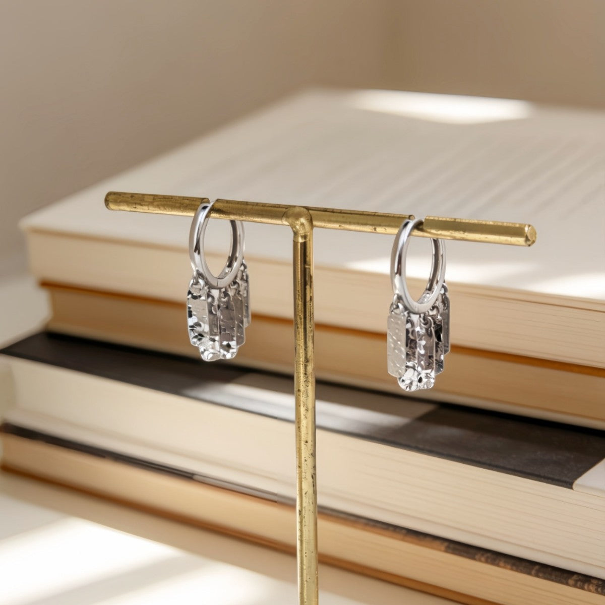 Silver Luma hammered fringe hoop earrings hanging from a stand