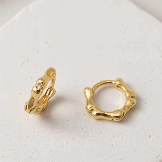 Gold Noma organic huggie earrings on a white background
