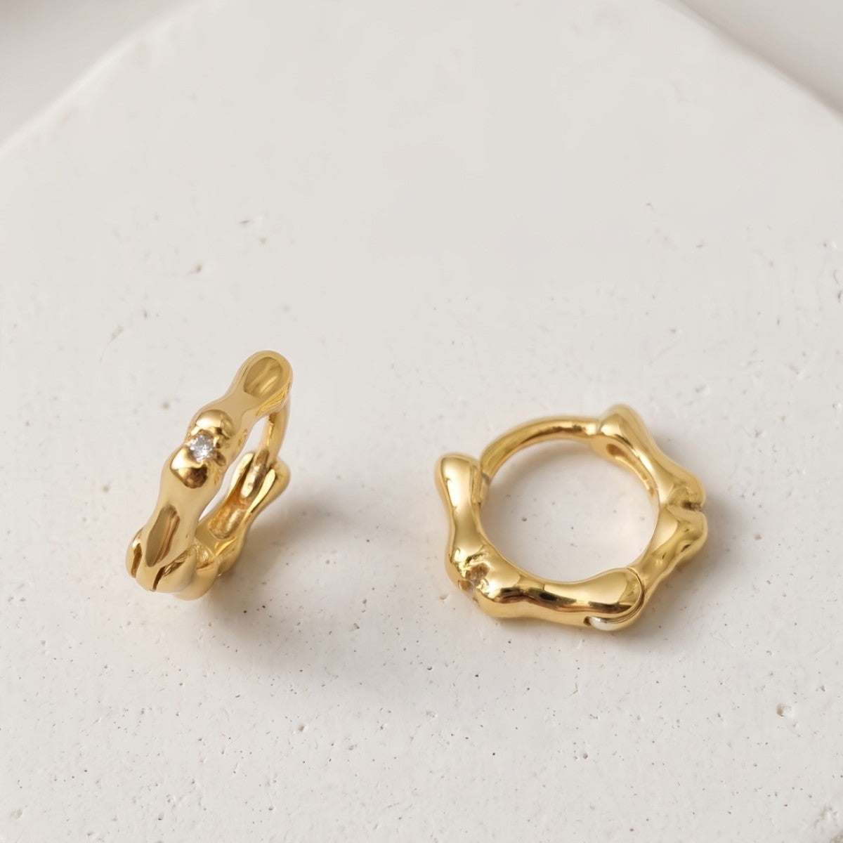 Gold Noma organic huggie earrings on a white background