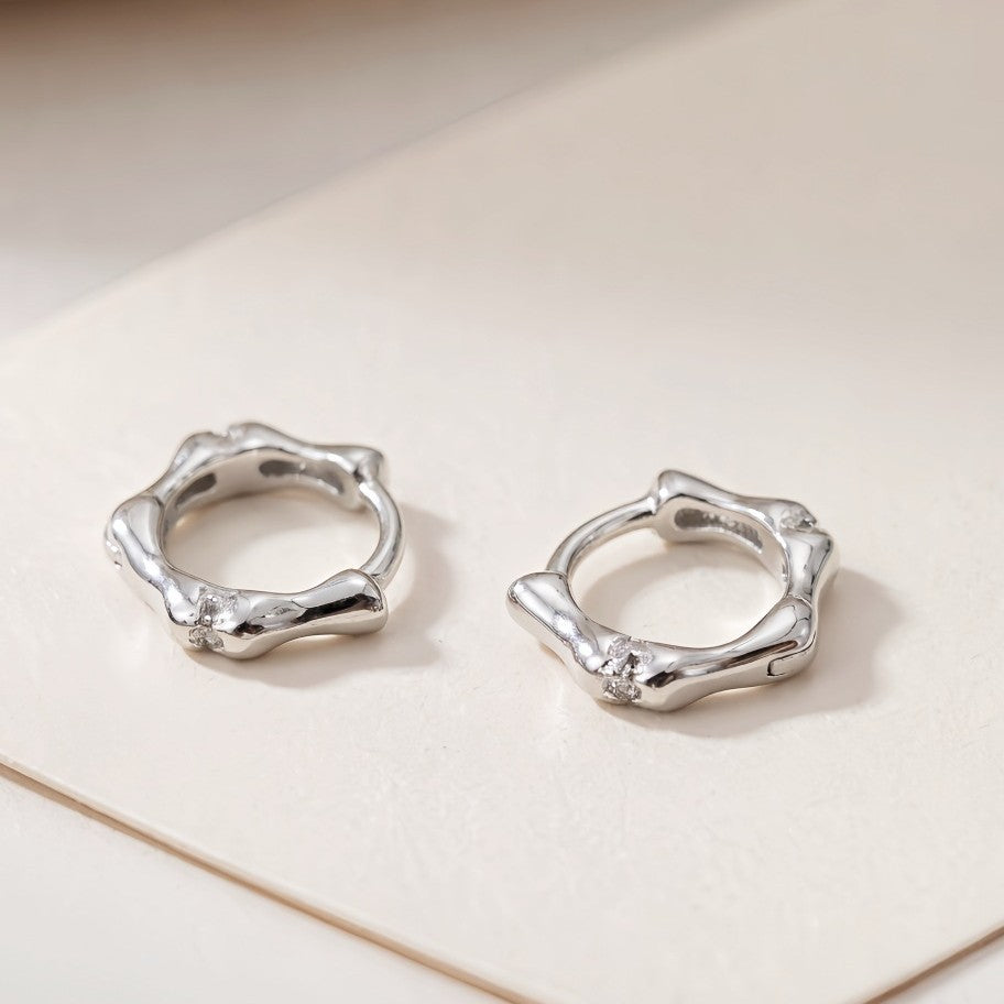 Silver Noma organic huggie earrings on a white background