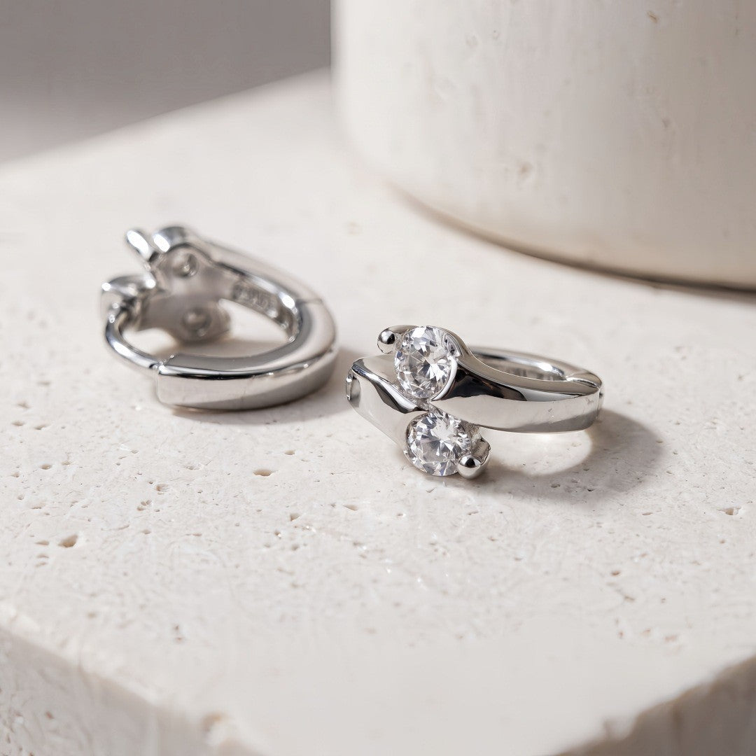 Silver Lumi double CZ huggie earrings on a light surface