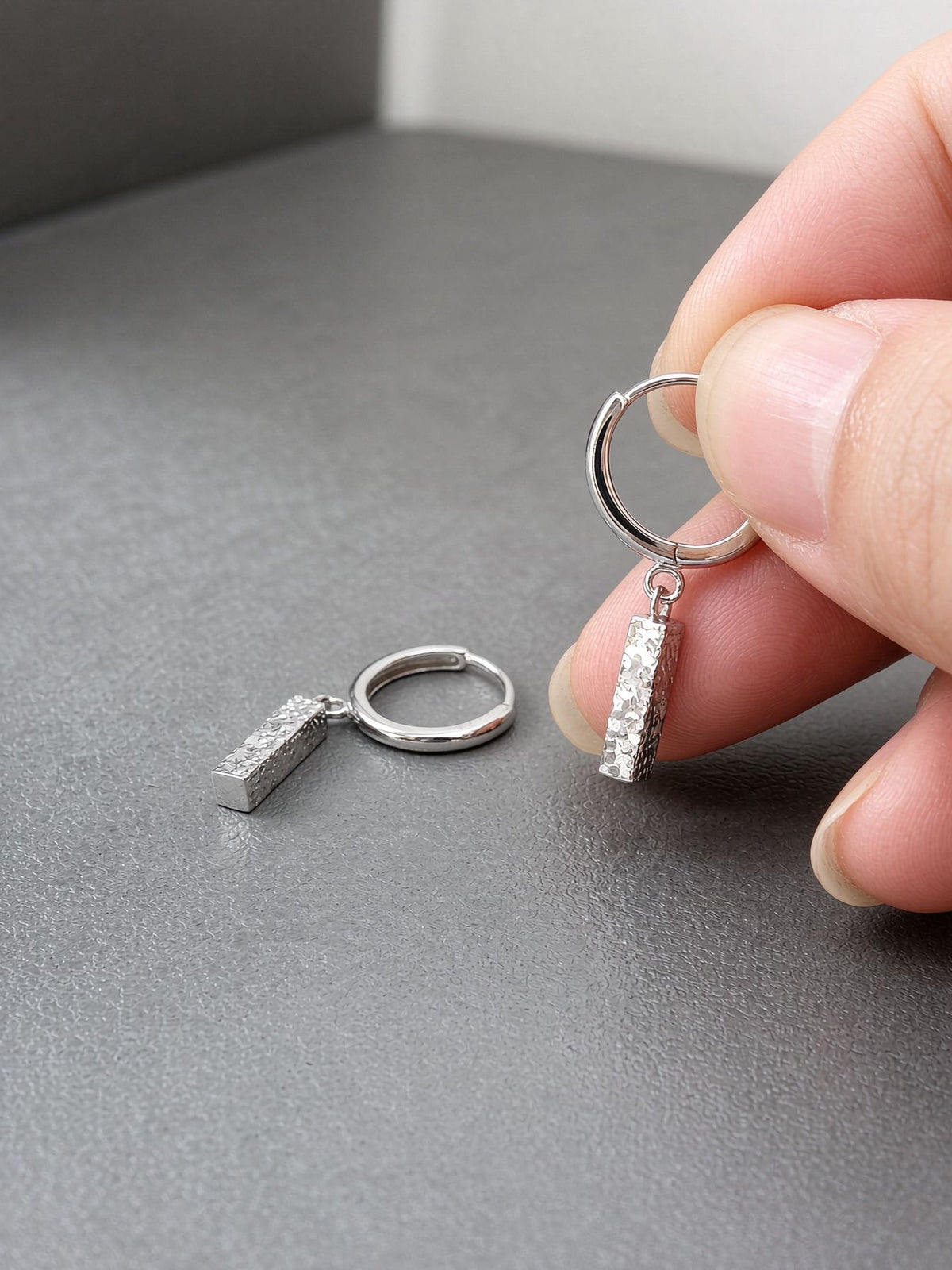 Silver Sora hammered bar drop earrings held between fingers