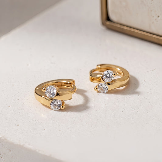 Gold Lumi double CZ huggie earrings on a white surface